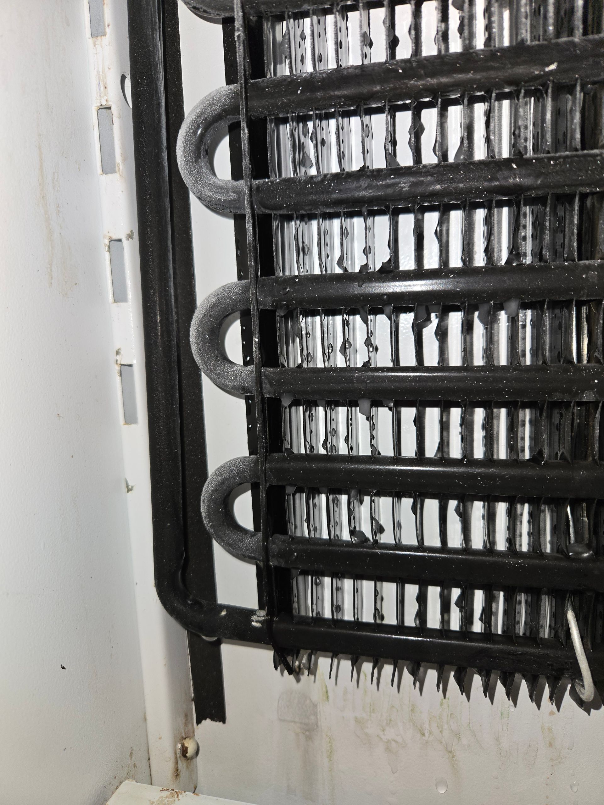 Close-up of a black radiator or cooling coil with bent pipes against a white wall