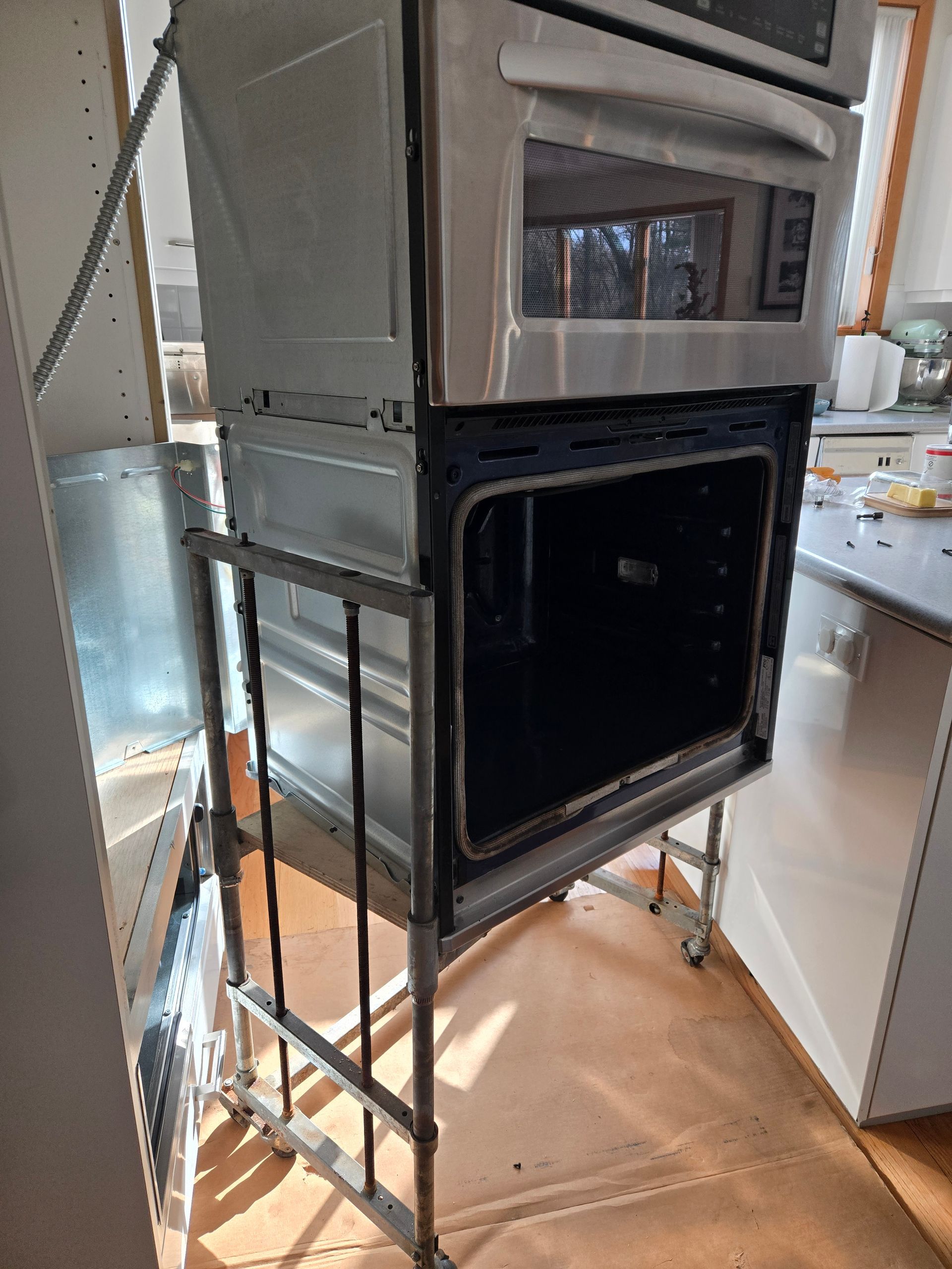 Stacked kitchen appliances on a metal cart in a store aisle, with cabinets and countertops in the background