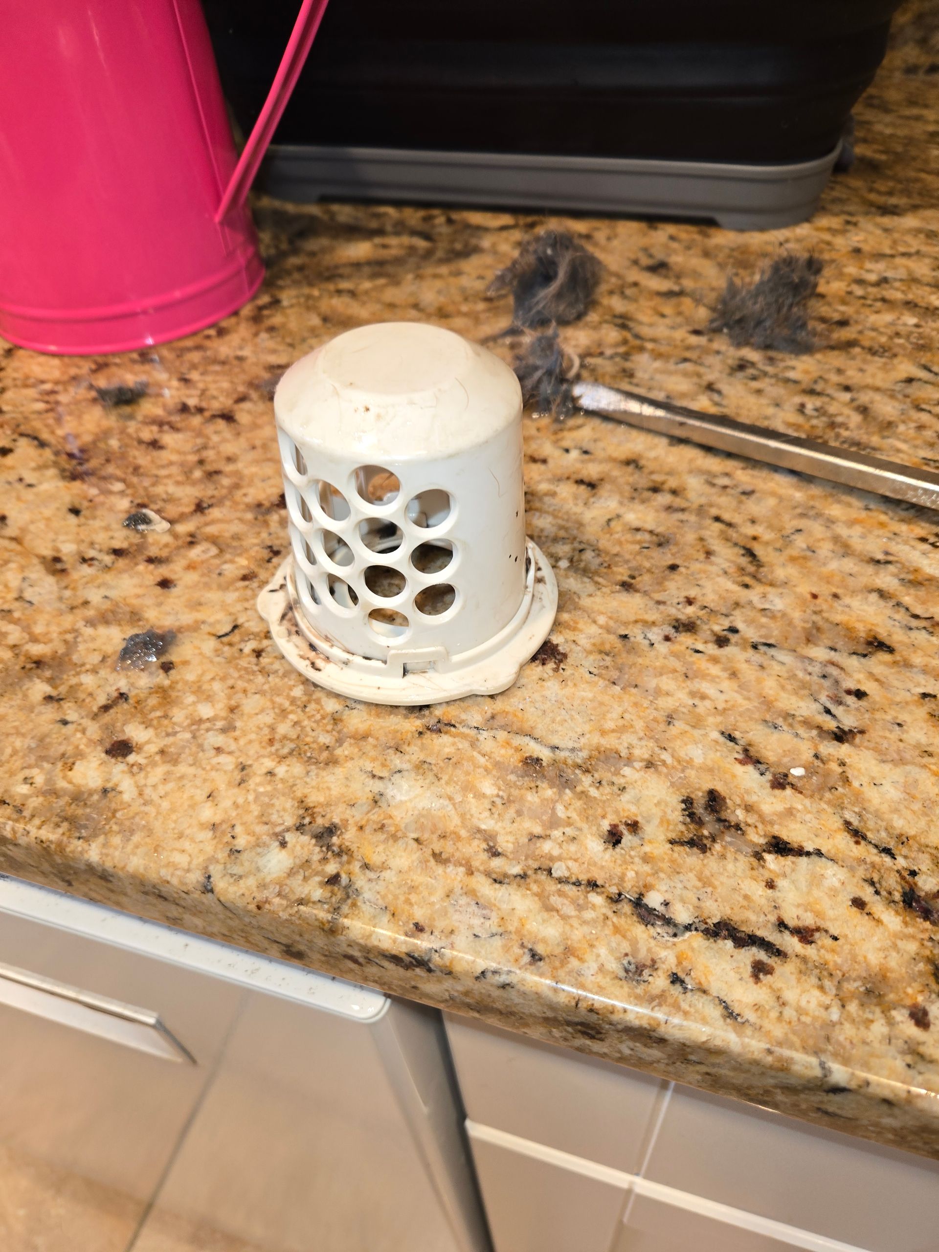 White perforated cup on granite kitchen counter next to pink container and dark utensil handle