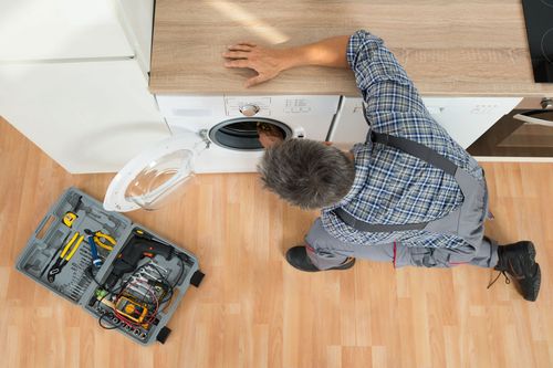 Person kneeling by a washing machine, working with tools and an open toolbox on the floor.