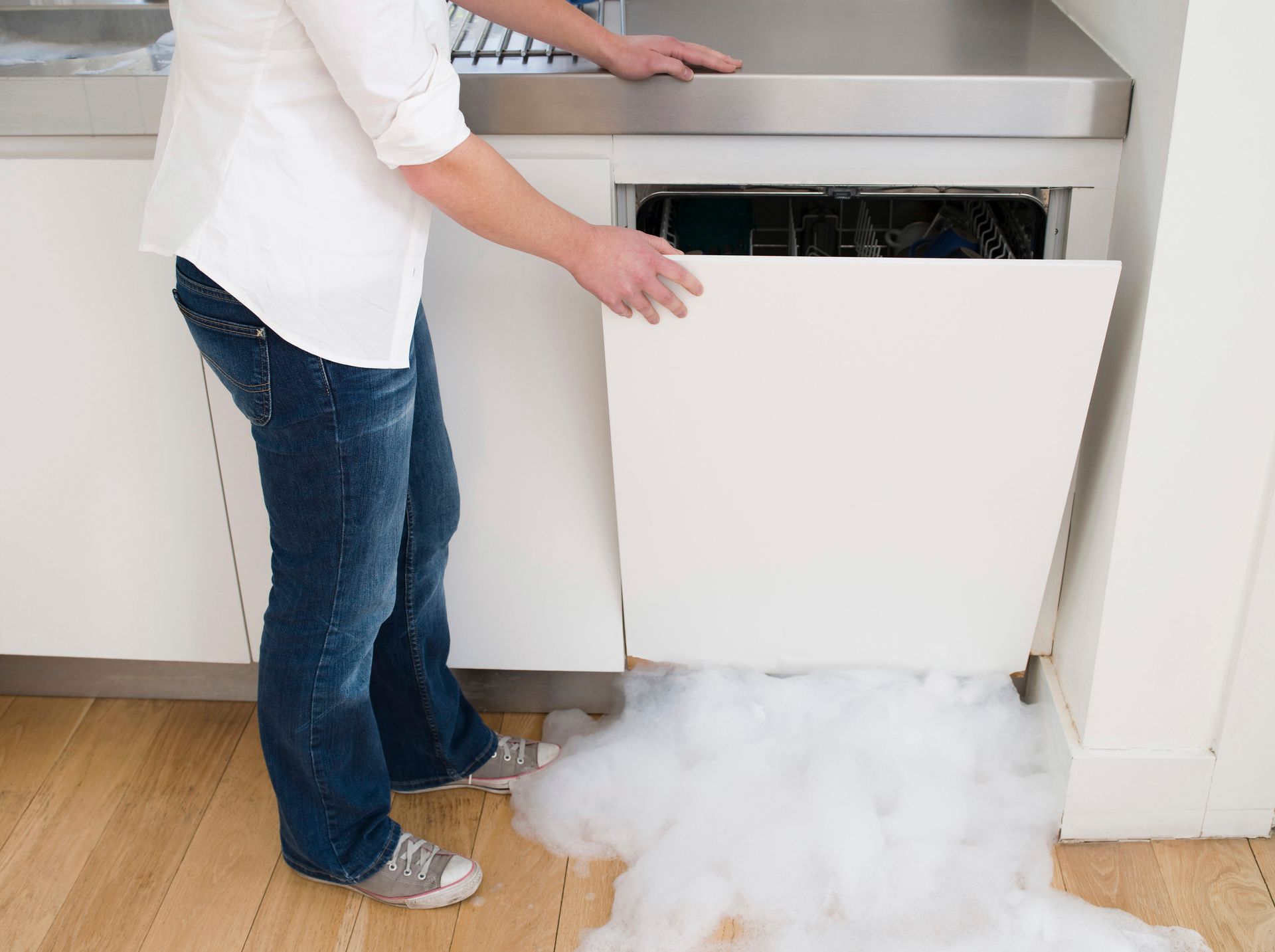 Person opening a dishwasher with foam spilling onto the kitchen floor
