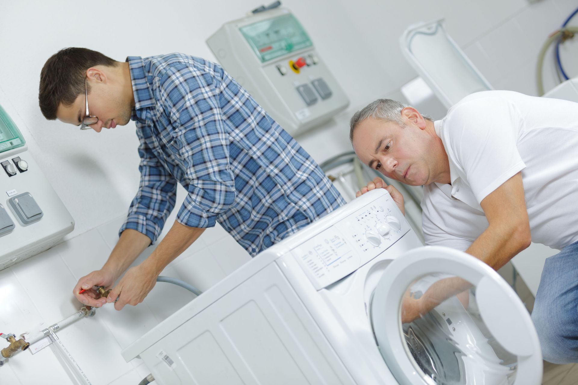 Two men repairing a front-loading washing machine in a bright laundry room
