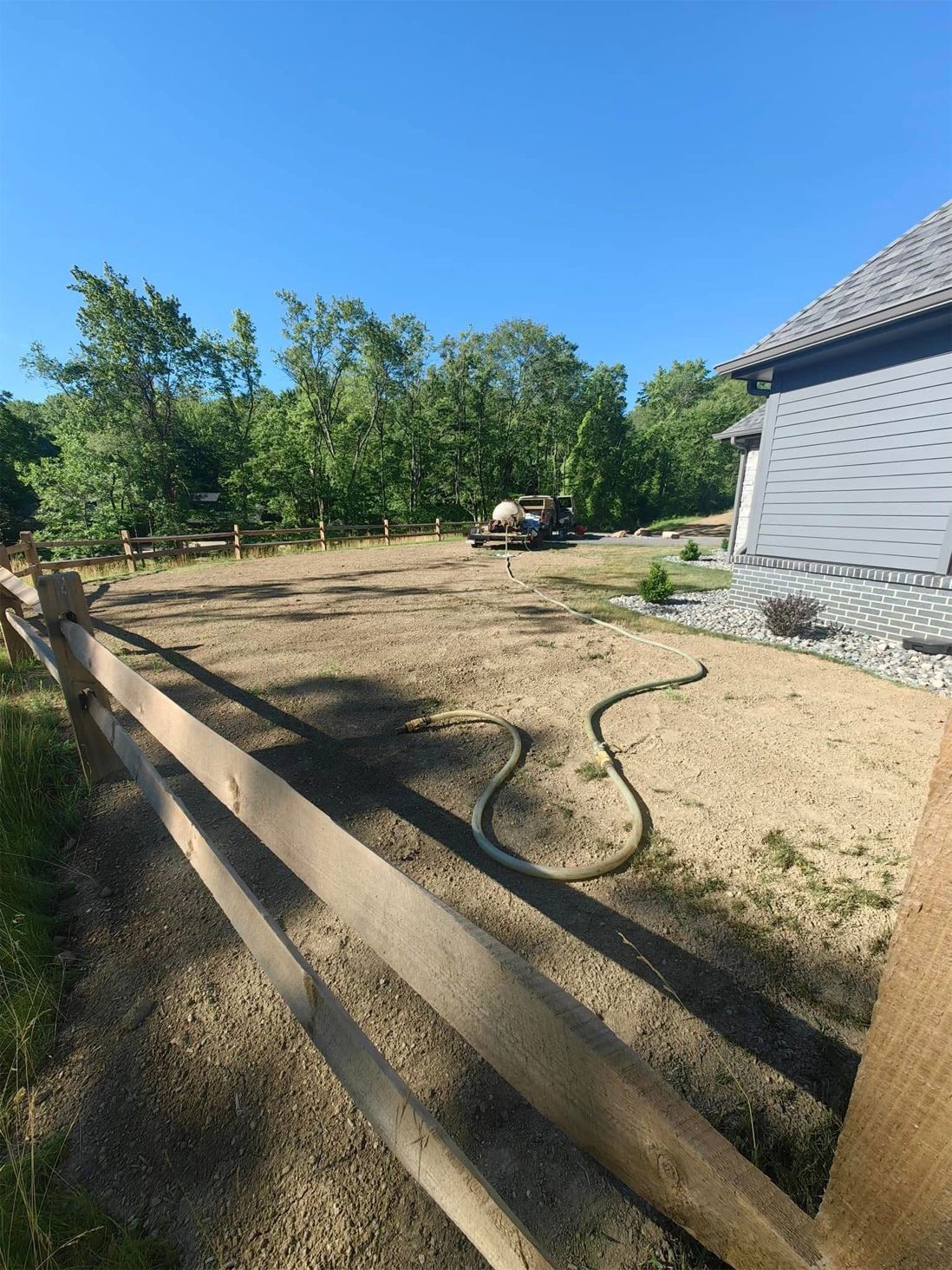 A freshly graded yard with a wooden fence, a hose, and a building under a blue sky.