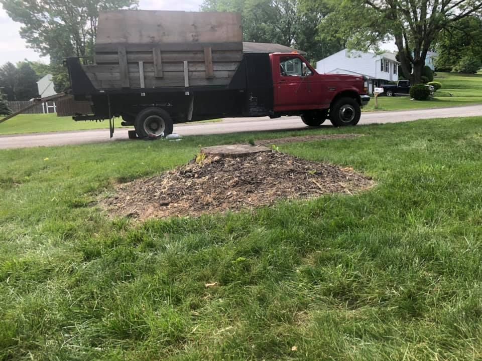 A red truck with a flatbed next to a pile of mulch on a grassy lawn.