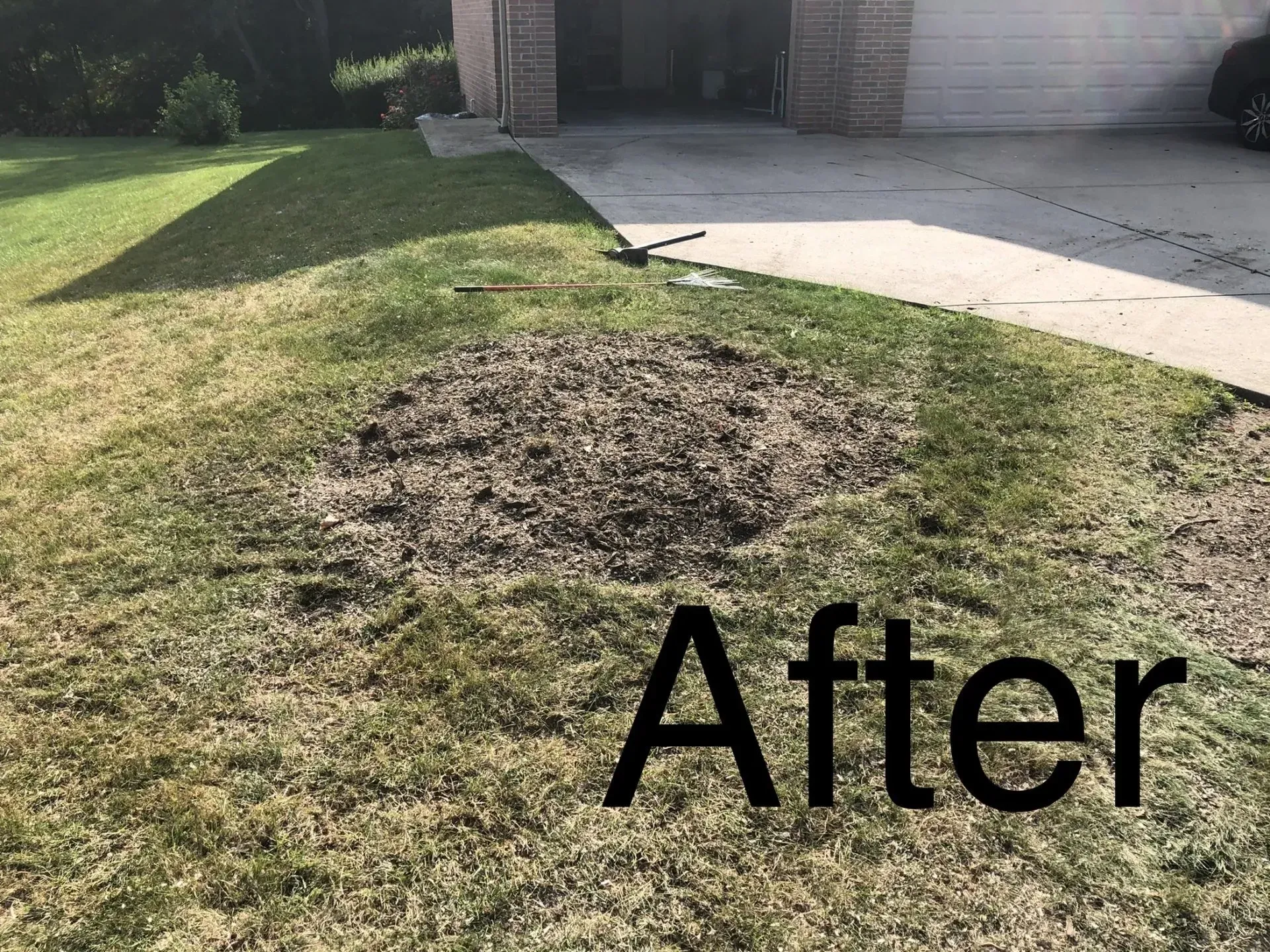 Lawn with a large bare patch after work. House and driveway are in the background. Green grass surrounding the bare area.