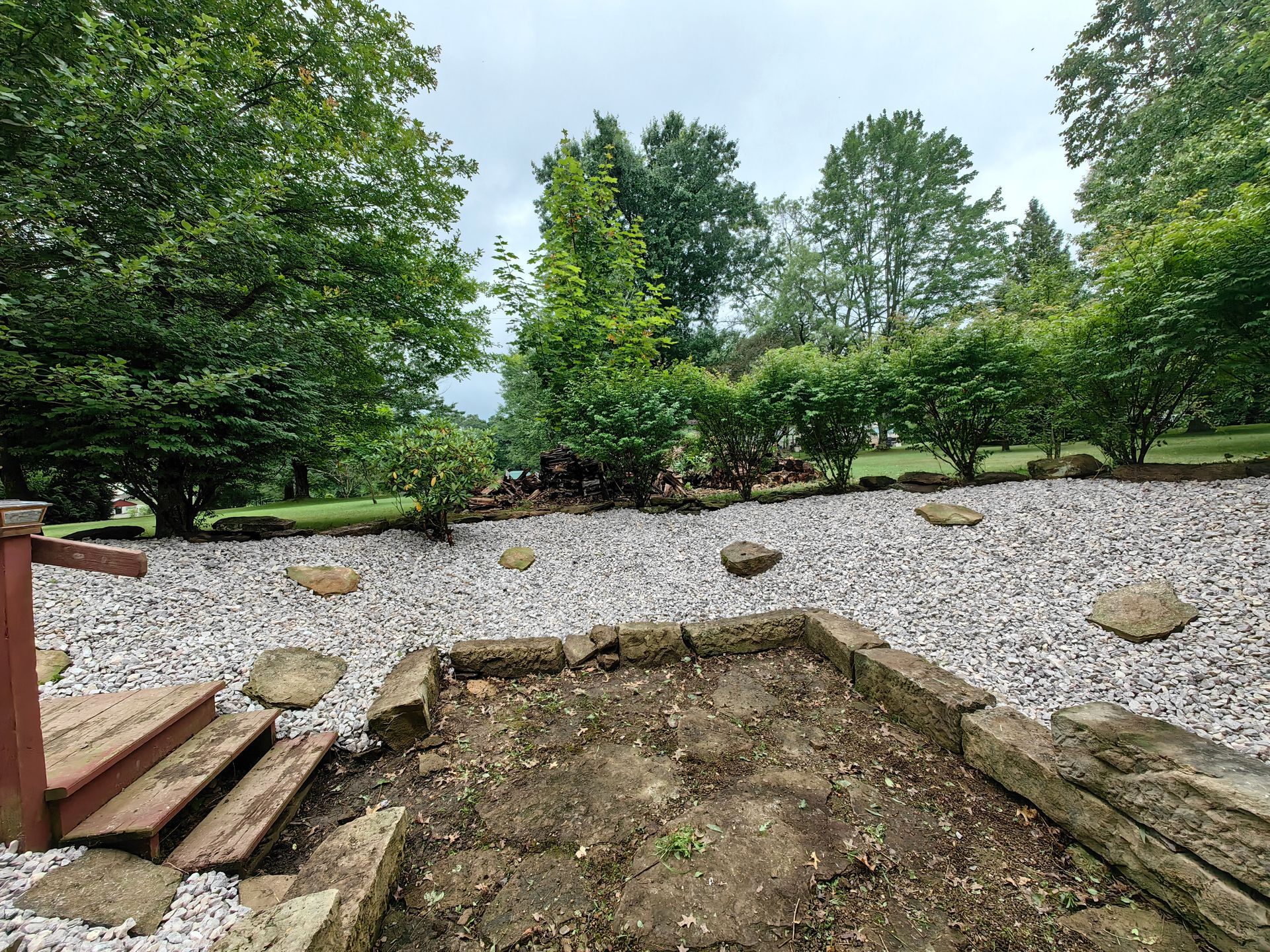 Backyard with rock bed, stepping stones, and lush greenery under a cloudy sky.