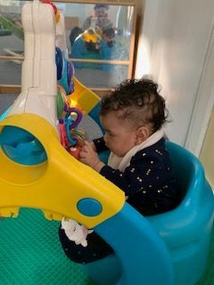 Baby in a blue activity center, playing with toys. Bright colors, indoors.