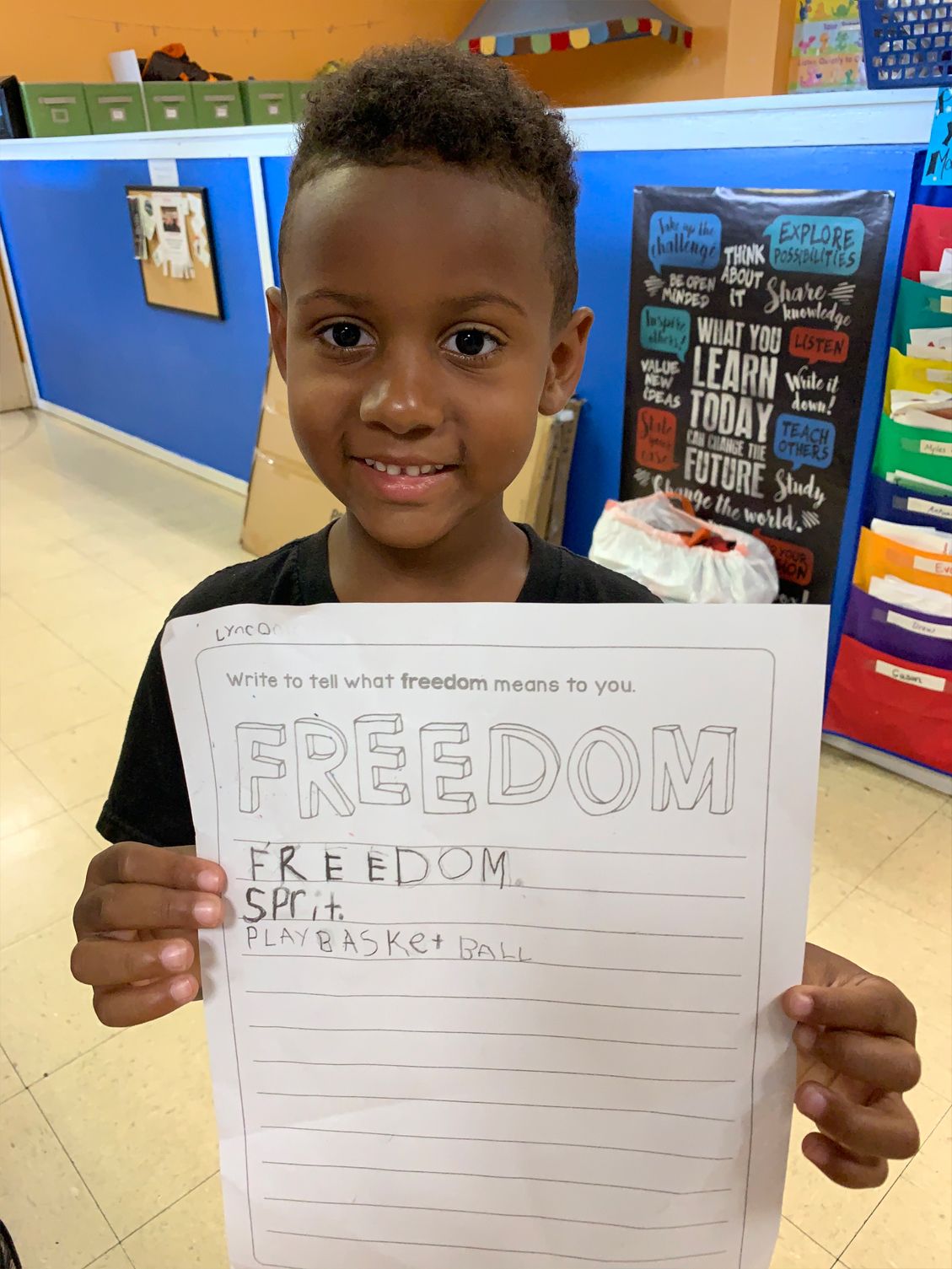 Boy holding a paper, smiling in a classroom setting.