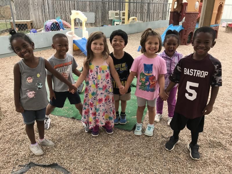 Children holding hands, smiling outdoors. Playground setting.