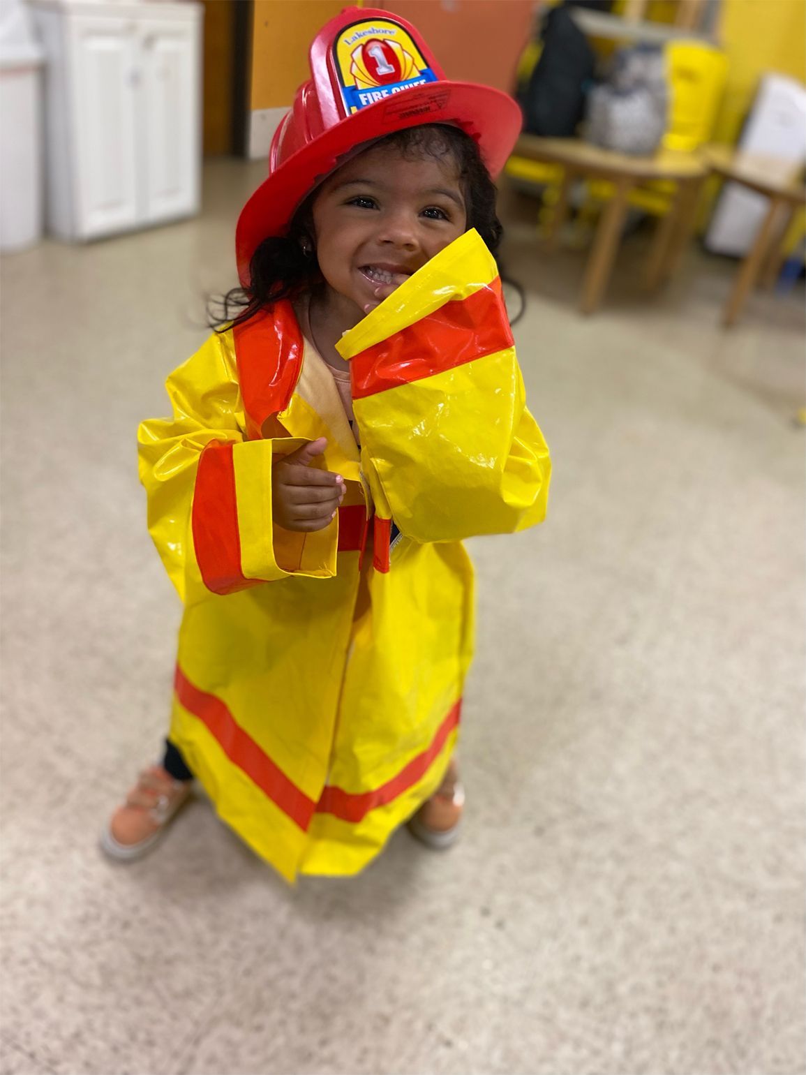 Child in yellow firefighter costume, smiling, holding a pretend tool.