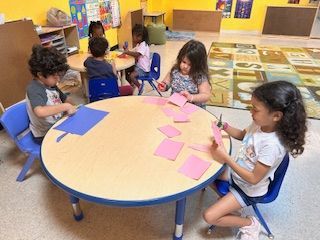 Children seated at tables cutting paper in a classroom.