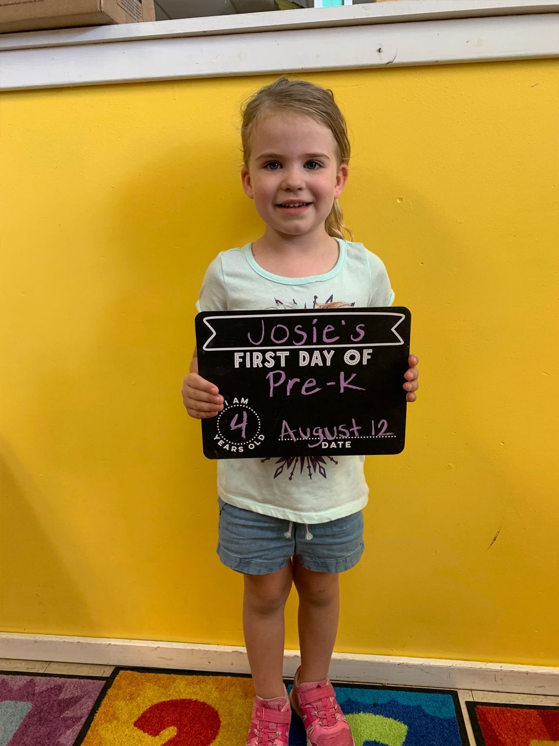 Girl holding a chalkboard standing in front of a yellow wall.