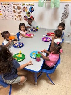 Children eating at a table in a brightly lit classroom.