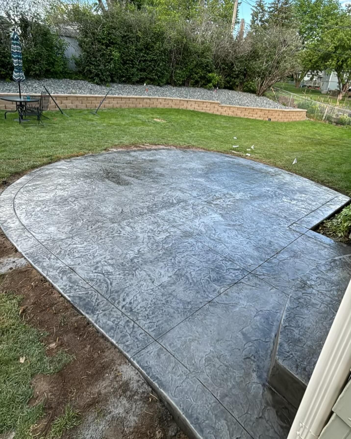 A concrete patio in a backyard with a table and chairs.