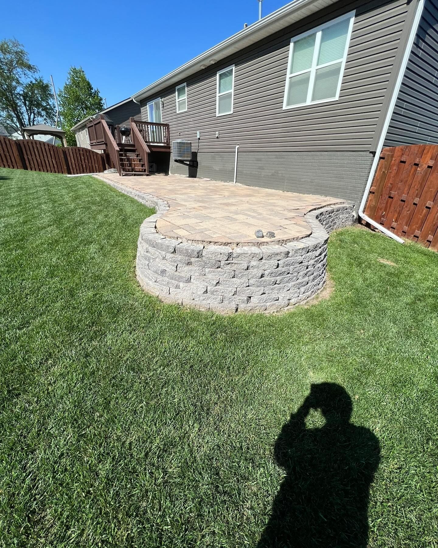 A shadow of a person is cast on the grass in front of a house.