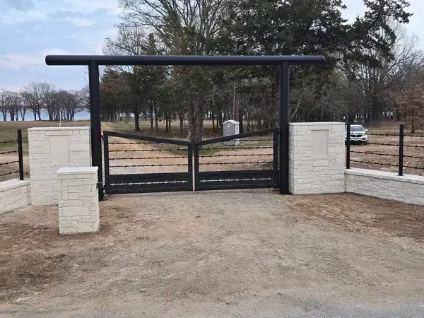 Black metal gate between white stone pillars at a rural driveway entrance