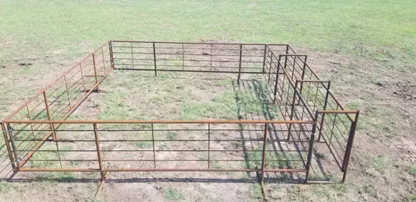 Rusty metal animal pen in a grassy field, with wire fencing and open ground inside.