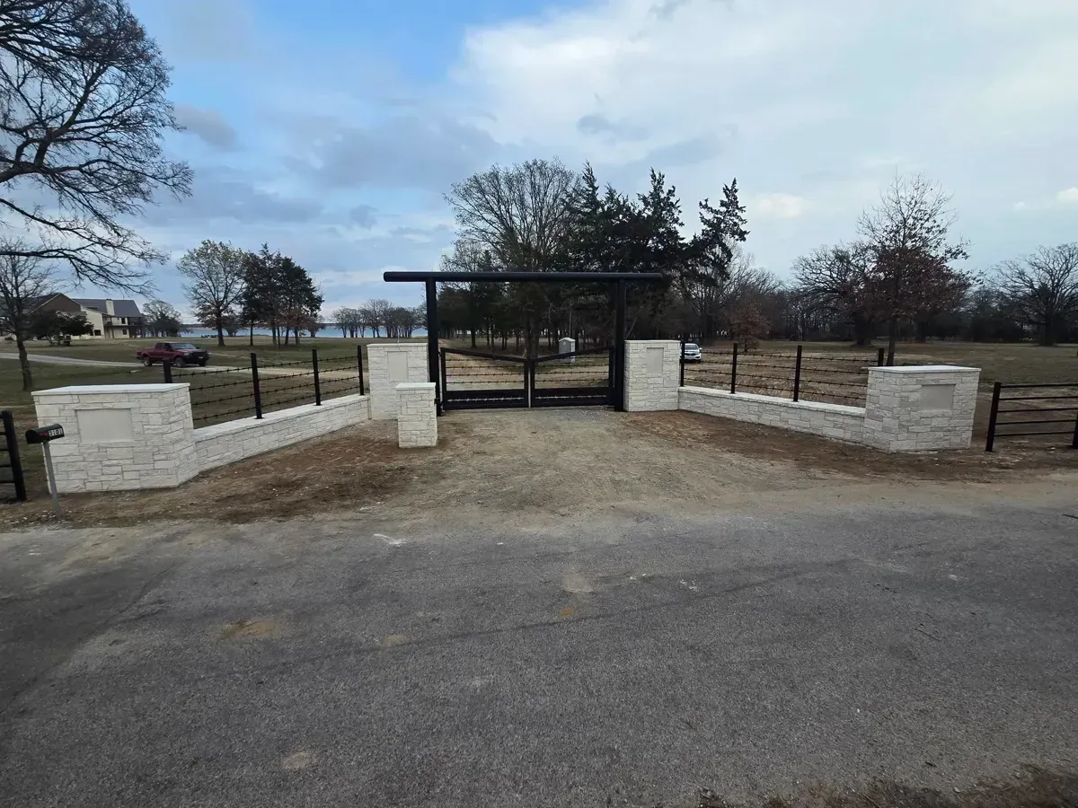 Park entrance with black metal gate and stone walls beside a paved road under a cloudy sky