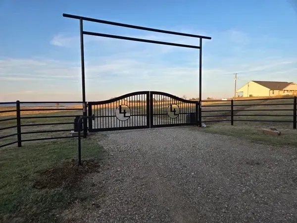 Rural gravel driveway leading to a black metal gate and fence at sunset