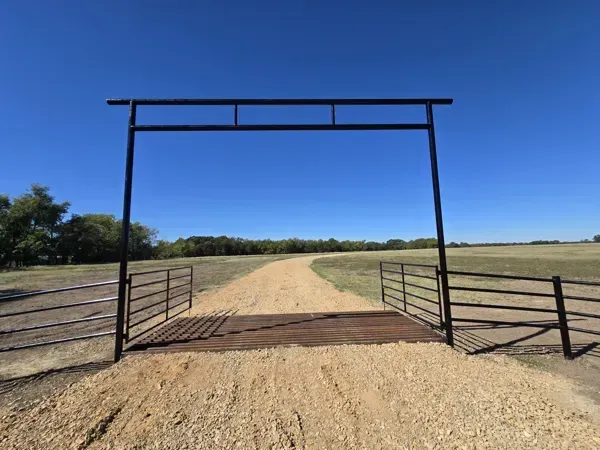 Rural dirt road through an open metal gate under a clear blue sky