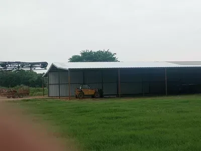 Small metal shed on a grassy field under an overcast sky, with a tractor parked beside it.