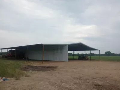 Open-sided metal farm shed in a rural field under a cloudy sky