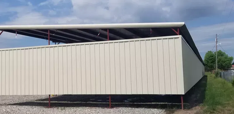 White modular building with a dark slanted roof beside a grassy roadside area