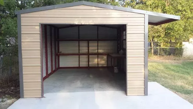 Small beige metal shed with an open front, concrete floor, and interior shelving