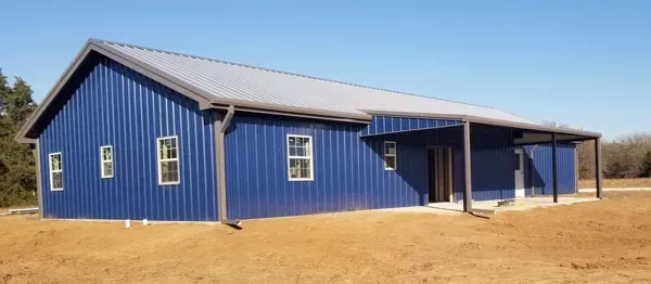 Blue metal house with a porch on a dry dirt lot under a clear sky