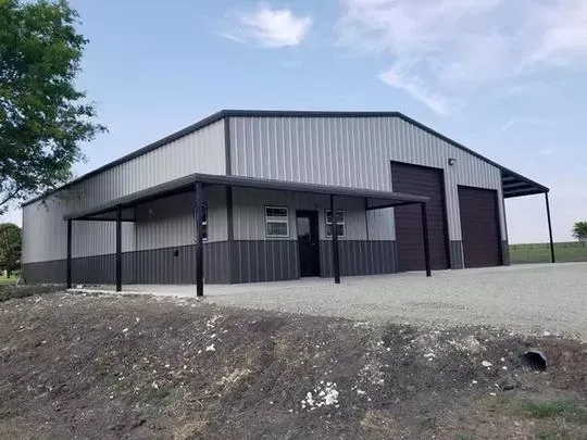 Gray metal barn with a covered porch on a gravel lot under a blue sky