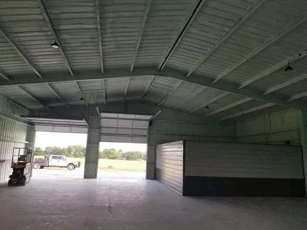 Empty warehouse interior with a forklift near the open entrance and a white trailer on the right.