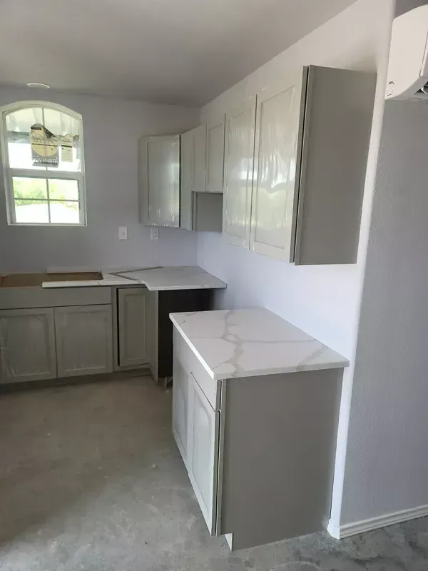 Small empty kitchen with gray cabinets, white countertops, and a window letting in natural light.