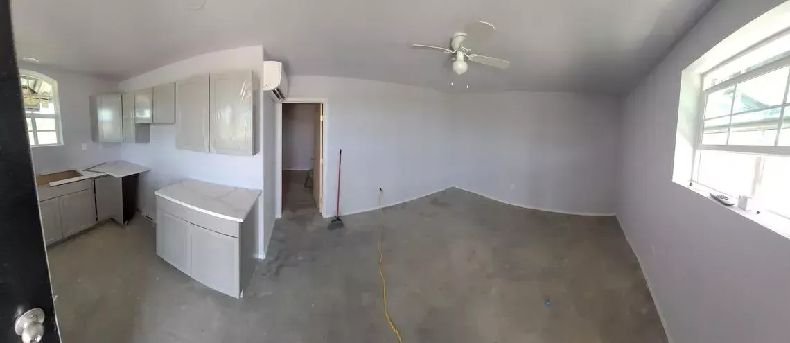 Empty unfurnished room with gray walls, white ceiling fan, and windows on two sides
