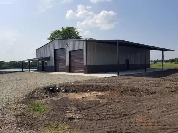 Gray metal warehouse with two garage doors on a gravel lot under a blue sky