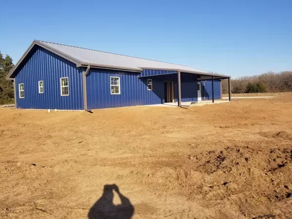 Blue metal house with porch on a bare dirt lot under a clear sky