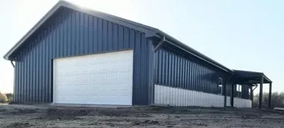 Blue metal barn with a large white garage door on a dirt lot