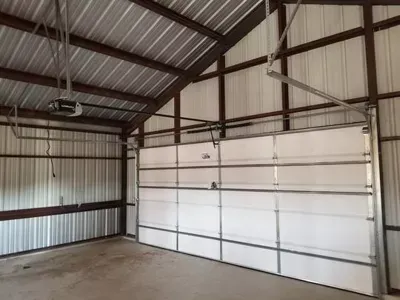Empty metal garage interior with a large white sectional door and concrete floor
