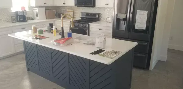 Modern kitchen island with white countertop, dark blue base, sink, and black refrigerator in the background