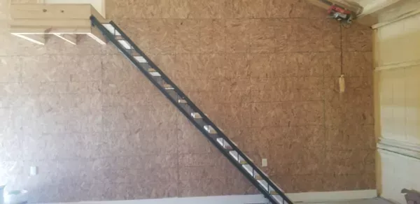 A long black ladder leaning against a tan wall in a room.