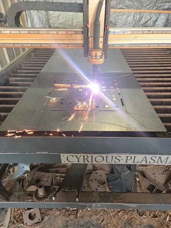 Plasma cutter cutting sheet metal on a CNC table, with bright sparks in an industrial workshop
