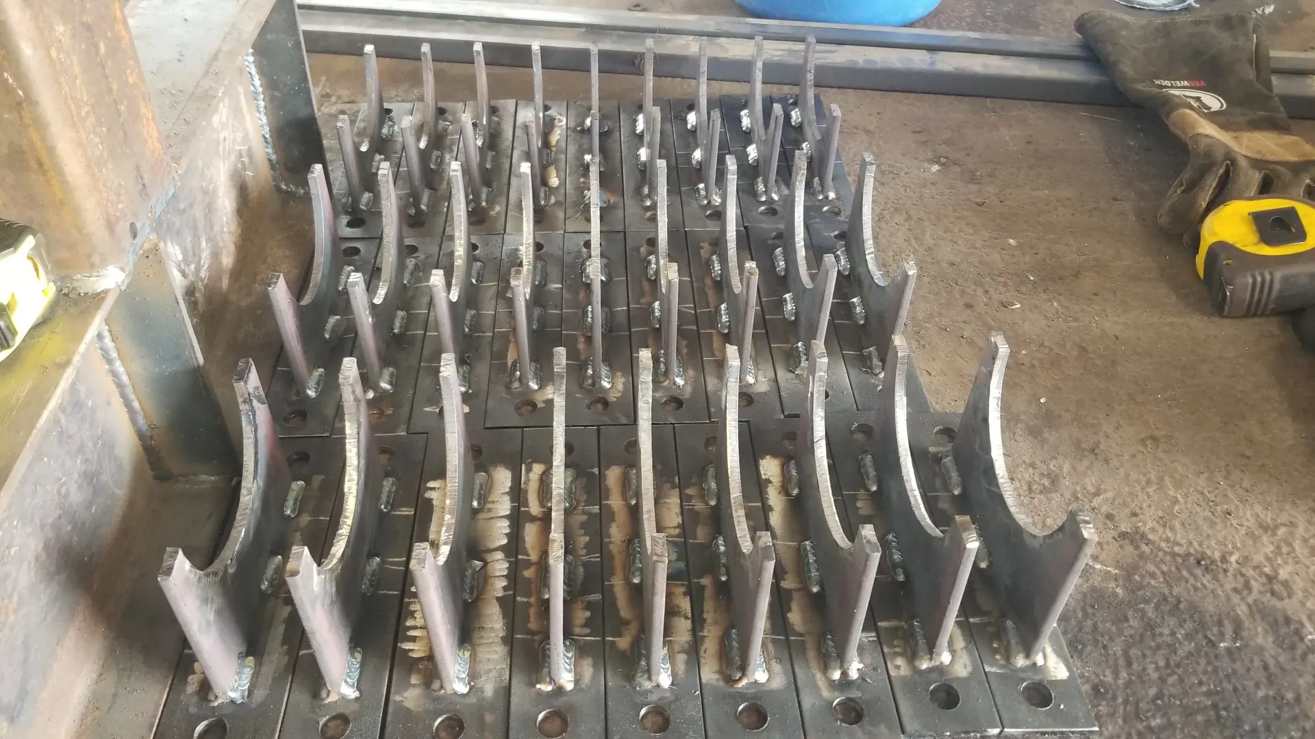 Rows of metal engine cylinder heads arranged on a workshop floor, with a yellow tool in the background.