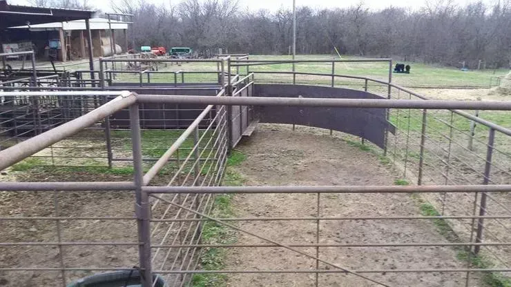 Rural park with metal railings over a dirt path and a small bridge near a grassy field