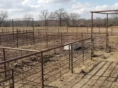 Rusty metal livestock pens in a dry field under a cloudy sky.
