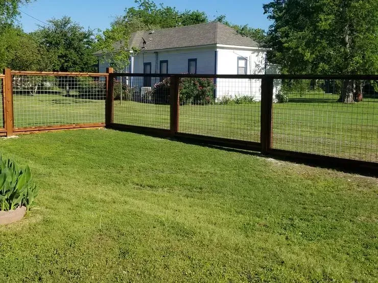 Small white shed in a grassy yard with a black-and-orange fence and trees in the background