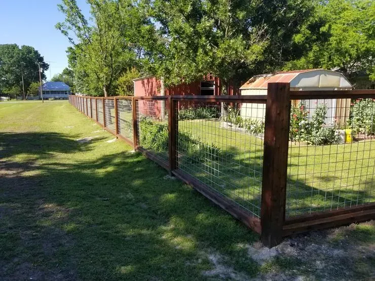 Wooden and wire fence along a grassy yard with trees and a house in the background