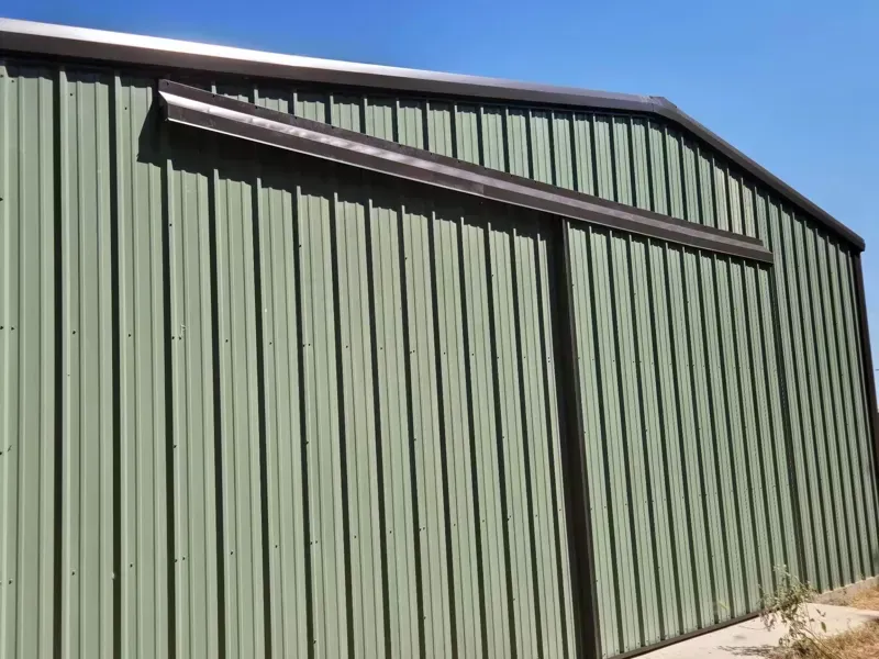 Green corrugated metal building with a slanted roof against a blue sky