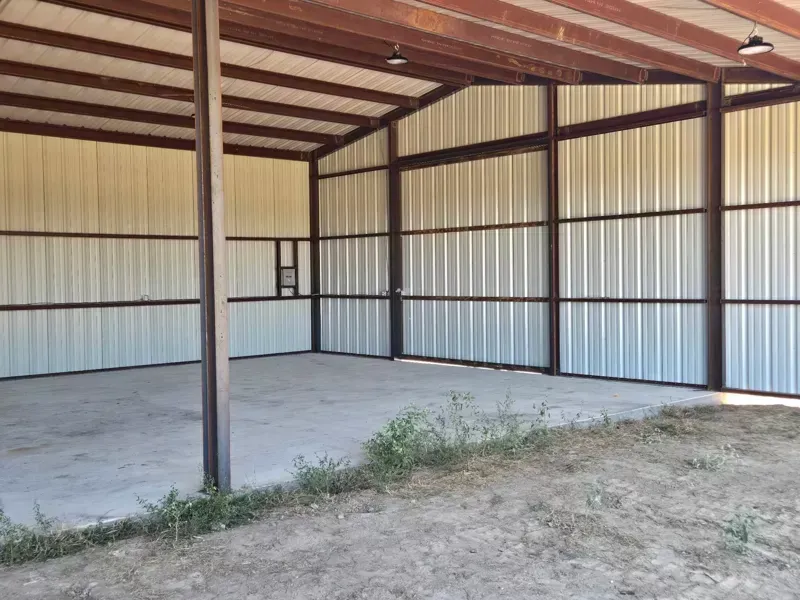 Empty metal storage shed with a concrete floor and dirt foreground, viewed from the open entrance