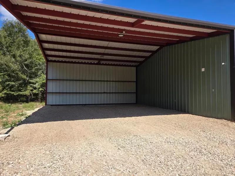 Open-sided metal carport with gravel floor and red roof, viewed from the front.