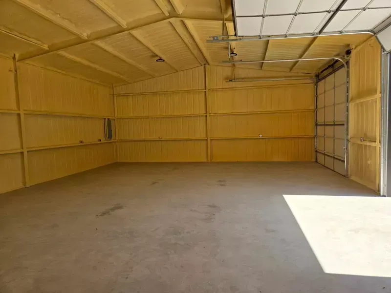 Empty yellow metal garage with a concrete floor and an open doorway creating a bright sunlit patch