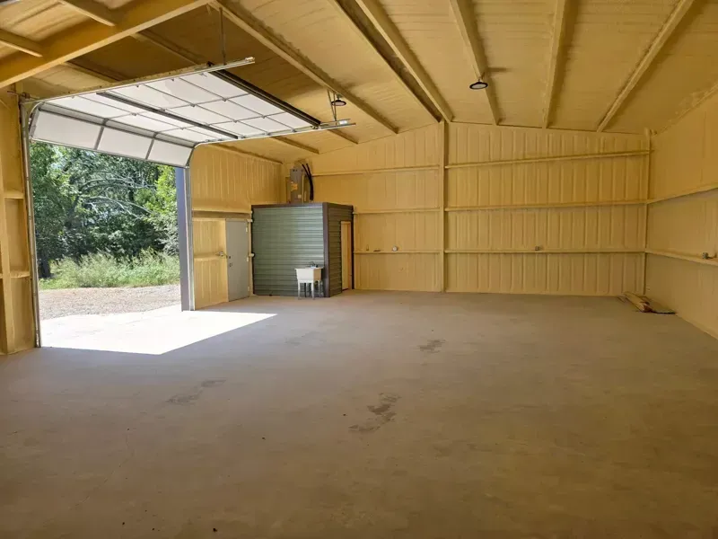 Empty tan metal warehouse interior with an open roll-up door and sunlight spilling onto the floor